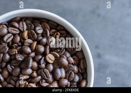 Nahaufnahme ganzer Kaffeebohnen in einem weißen Becher auf grauem Hintergrund; Draufsicht Stockfoto