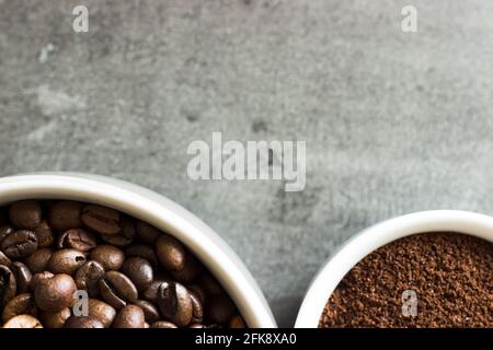 Nahaufnahme ganzer Kaffeebohnen und gemahlener Kaffeebohnen auf grauem Hintergrund in weißen Tassen mit Kopierfläche; Draufsicht Stockfoto