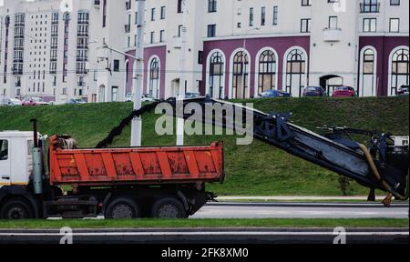 Straßenfräsmaschine entfernt alten Asphalt und lädt gefrästen Asphalt in den Muldenkipper. Reparaturprozess. Stockfoto
