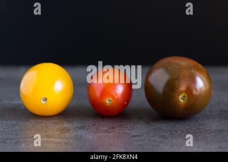 Nahaufnahme von drei bunten kleinen Tomaten auf dunklem Hintergrund; buntes Gemüse Stockfoto