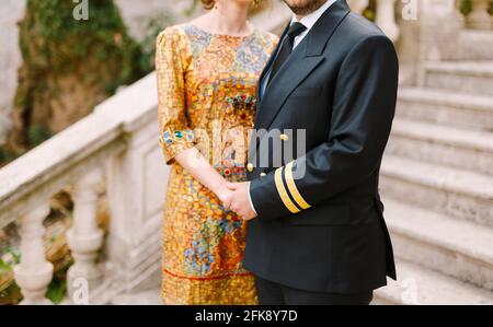 Die Braut in einem ungewöhnlichen Kleid mit einer Ikone und Der Bräutigam in einem Anzug umarmt das Alte Treppen vor der Hochzeit Stockfoto