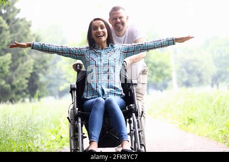 Guy trägt freudige Frau im Rollstuhl Nahaufnahme Stockfoto
