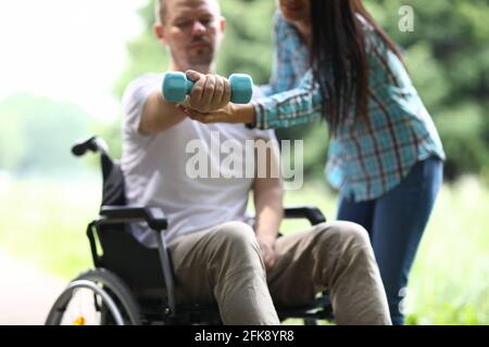 Frau hilft Mann im Rollstuhl, Übungen mit Hanteln zu machen Stockfoto