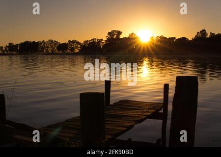 Sonnenuntergang am See Lobos, Buenos Aires. Vom Ufer aus mit Blick auf einen alten, kurzen hölzernen Pier und den See Stockfoto
