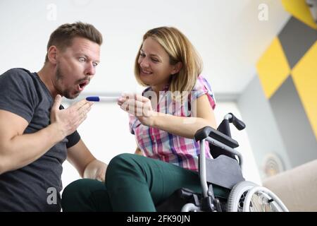 Freudige Frau im Rollstuhl zeigt überrascht Mann Schwangerschaftstest Stockfoto