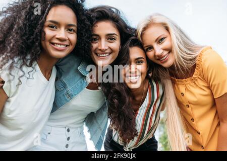 Gruppe von glücklichen jungen Frauen, die zusammen stehen und sich anguckend Kamera Stockfoto