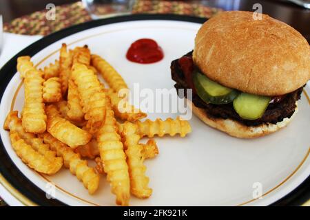 Nahaufnahme eines Hamburgers und Pommes auf einem Teller, mit einem Klecks Ketchup. Stockfoto