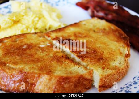 Nahaufnahme einer Scheibe Toast auf einem Teller, Speck und Rührei im Hintergrund unscharf. Stockfoto