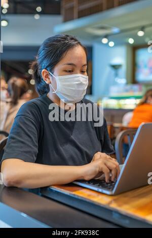 Vertikales Porträt einer Frau mit Schutzmaske und Laptop Stockfoto