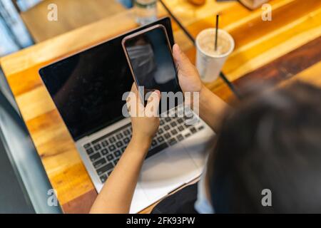 Rückansicht der Frau mit Smartphone und Laptop Stockfoto
