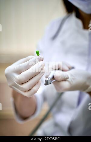 Die Hand des Zahnarztes in weißem Handschuh hält das Instrument, die Bor-Maschine. Zahnarztinstrument auf dem Hintergrund der Lichtklinik. Nahaufnahme. Stockfoto