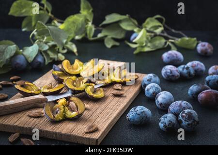 Pflaumen: Geschnittene reife Pflaumen und ganze Früchte auf einem Holzbrett, dunkler Hintergrund Stockfoto