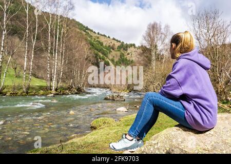 Portrait junge kaukasische Frau, die auf einem Felsen neben dem Fluss in einer Waldlandschaft sitzt.Frau genießt und ruht in der Natur. Stockfoto