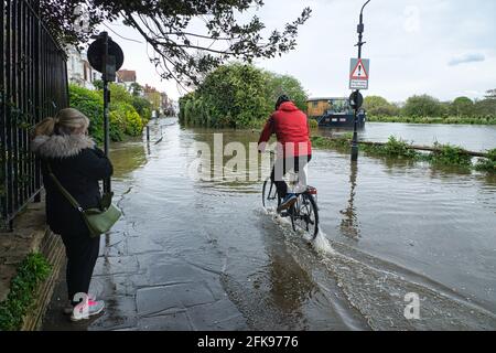 London, Großbritannien. April 2021. Die Chiswick Mall überflutet die Flut. Die Straße entlang der Chiswick Mall wird von außergewöhnlich hoher Flut überflutet, wenn Radfahrer absteigen und Fahrzeuge ein Wachen hinterlassen. Kredit: Peter Hogan/Alamy Live Nachrichten Stockfoto