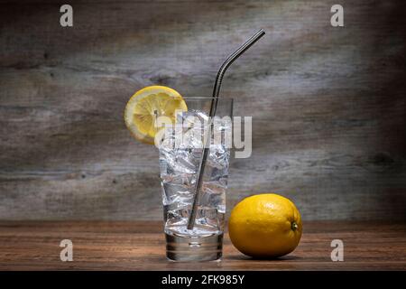 Glas Wasser mit Eis und Zitrone und einem Strohhalm aus Edelstahl in einem Longdrinkglas. Stockfoto