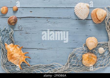 Muscheln und Fischernetz auf blauem Holzhintergrund. Urlaubs- und Urlaubskonzept. Stockfoto