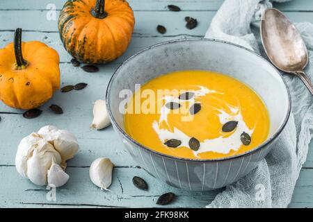 Kürbissuppe mit Creme und Kürbiskernen auf hellblauem rustikalem Holzhintergrund, verziert mit kleinen Kürbissen und Knoblauch Stockfoto