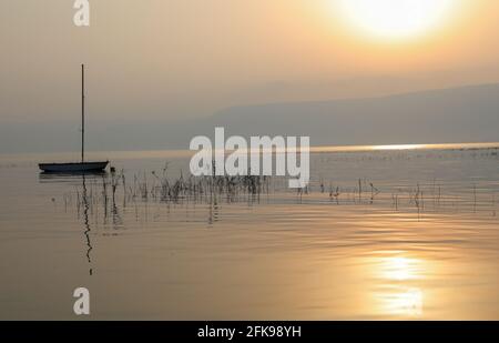 Sonnenaufgang über dem See. Boot schwimmt auf dem ruhigen Wasser unter herrlichem Sonnenuntergang. Stockfoto