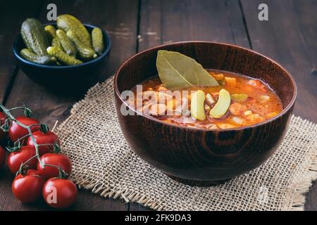 Schüssel mit Soljanka, einer würzigen und sauren Suppe russischen Ursprungs, auf dunklem Holztisch. Soljanka ist in den osteuropäischen Ländern und in Ostdeutschland beliebt. Stockfoto