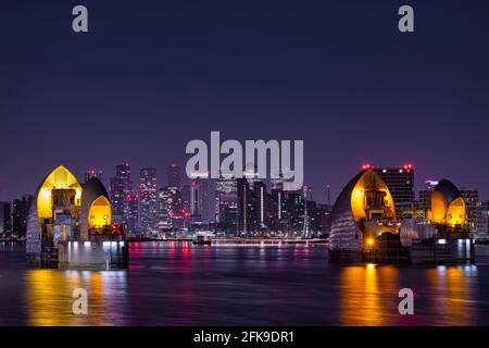 Die Thames Barrier bei Nacht mit der Isle of Dogs und Canary Wharf im Hintergrund. Stockfoto