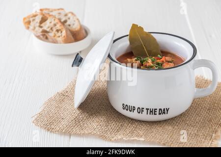 Schüssel mit Soljanka, einer würzigen und sauren Suppe russischen Ursprungs, auf weißem Holztisch. Soljanka ist in den osteuropäischen Ländern und in Ostdeutschland beliebt. Stockfoto