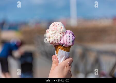 Rosafarbenes und weißes Eis in einem Kegel, das in der Sonne schmilzt. Stockfoto