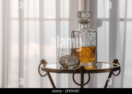 Whisky-Glas-Dekanter mit Whisky-Spirituosen und zwei Gläsern Mit Eisfelsen auf einem Glastisch in gemütlicher Hoteleinrichtung Stockfoto