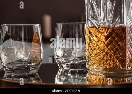 Whisky-Glas-Dekanter mit Whisky-Spirituosen und zwei Gläsern Mit Eisfelsen auf einem Glastisch in gemütlicher Hoteleinrichtung Stockfoto