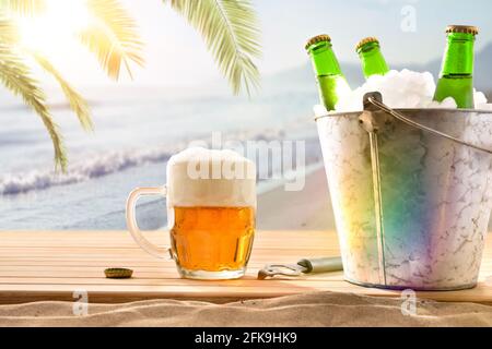 Bierkrug und Eiskübel mit Bierflaschen gefüllt Holzsockel und Strandhintergrund mit Palmen Stockfoto