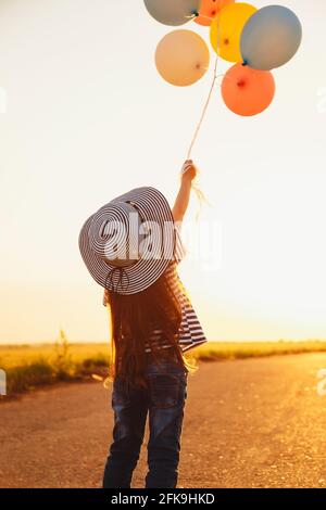 Kleines Mädchen auf der Straße spielt mit bunten Ballons bei Sonnenuntergang Stockfoto