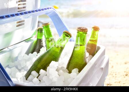 An einem heißen Tag mit Sonnenschein in einem Campingkühlschrank am Strand gekühlte Bierflaschen auf Eis. Stockfoto