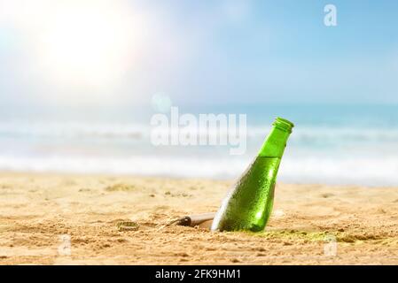 Detail der frischen Bierflasche, die an einem heißen Tag im Sand am Strand halb vergraben ist. Vorderansicht. Stockfoto