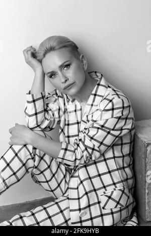 Elegante und charismatische blonde und kurzhaarige Frauen mit einem schönen breiten Lächeln in einem übergroßen Leinenanzug, der isoliert im Studio posiert. Schwarz und Weiß Stockfoto