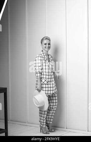 Elegante und charismatische blonde und kurzhaarige Frauen mit einem schönen breiten Lächeln in einem übergroßen Leinenanzug, der isoliert im Studio posiert. Schwarz und Weiß Stockfoto