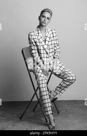 Elegante und charismatische blonde und kurzhaarige Frauen mit einem schönen breiten Lächeln in einem übergroßen Leinenanzug, der isoliert im Studio posiert. Schwarz und Weiß Stockfoto