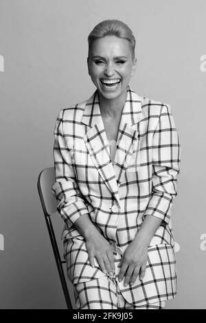 Elegante und charismatische blonde und kurzhaarige Frauen mit einem schönen breiten Lächeln in einem übergroßen Leinenanzug, der isoliert im Studio posiert. Schwarz und Weiß Stockfoto