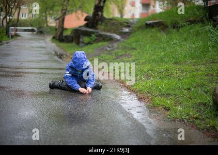 Kind sitzt auf dem Boden bei regnerischem Wetter Abholung Ein Regenwurm Stockfoto