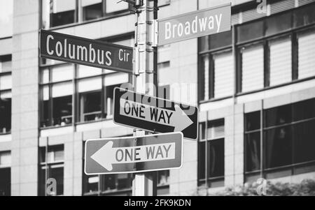 Schwarz-Weiß-Bild eines Postes mit Columbus Circle, Broadway- und Einbahnstraßen-Schildern, selektiver Fokus, New York City, USA. Stockfoto