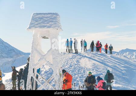 Kasprowy Wierch, Polen 28.01.2021 - EINE Gruppe von Wanderern auf einem verschneiten Berggipfel. Nahaufnahme Blick auf einen verschneiten Glockenturm. Landschaftlich klarer weißer Himmel im Hintergrund. Menschen, die Fotos von der Aussicht machen. Stockfoto