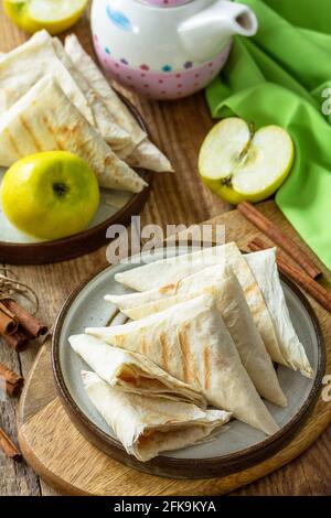 Apfelgebäck zum Frühstück. Gegrilltes Lavash-Dreieck mit Äpfeln und Zimt auf einem Holztisch. Stockfoto