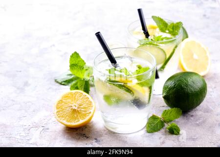 Zwei Gläser erfrischendes alkoholfreies Mojito Limonade-Getränk mit Bio-Zitrone, Limettenscheiben, Minzblättern, Stroh, Eiswürfeln auf grunziertem grauen Beton Stockfoto