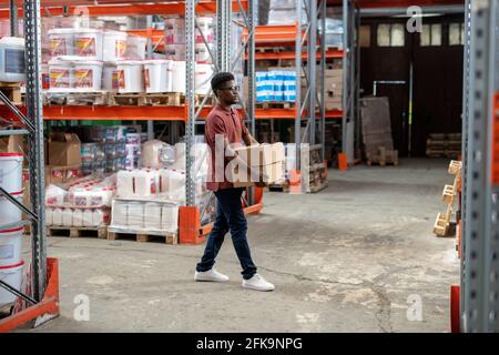 Ernst junge schwarze Kerl in Freizeitkleidung tragen Pappkartons Im Lager oder im Hardwaremarkt Stockfoto