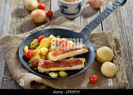 Gebratene bayerische Würstchen, sogenannte Wollwurst, eine Spezialität ähnlich der deutschen Kalbswurst, aber ohne Gehäuse, auf Bratkartoffeln mit Speck Stockfoto