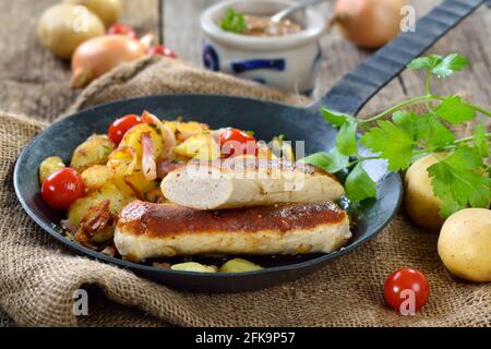 Gebratene bayerische Würstchen, sogenannte Wollwurst, eine Spezialität ähnlich der deutschen Kalbswurst, aber ohne Gehäuse, auf Bratkartoffeln mit Speck Stockfoto