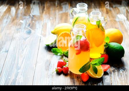 Drei Jahrgangsflaschen frischer, eiskalter Limonade, verschiedene Geschmacksgetränke mit Zitrone, Orange, Grapefruit, Limette, Minzblättern & Erdbeere auf grunged Woode Stockfoto