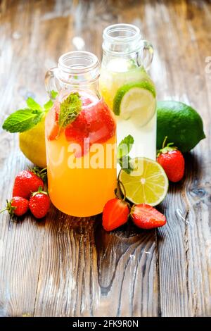 Drei Jahrgangsflaschen frischer, eiskalter Limonade, verschiedene Geschmacksgetränke mit Zitrone, Orange, Grapefruit, Limette, Minzblättern & Erdbeere auf grunged Woode Stockfoto