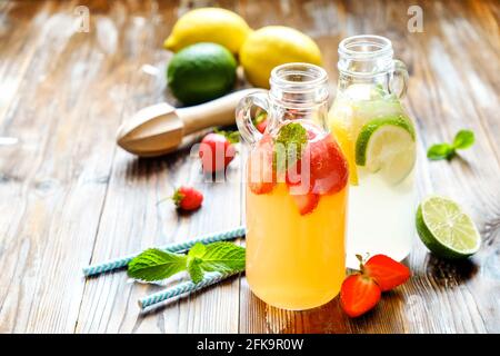 Drei Jahrgangsflaschen frischer, eiskalter Limonade, verschiedene Geschmacksgetränke mit Zitrone, Orange, Grapefruit, Limette, Minzblättern & Erdbeere auf grunged Woode Stockfoto