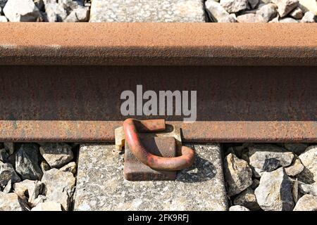 Nahaufnahme einer Schwermetallklammer, die eine Eisenbahnstrecke an einem Betonschwellen befestigt. Keine Personen. Stockfoto