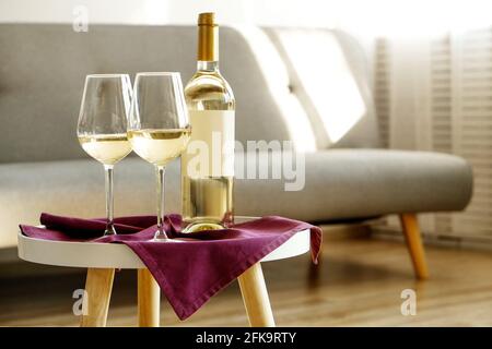 Vintage-Flasche Weißwein mit leerem mattem Etikett und zwei Gläsern auf violetter Serviette, luftiger Innenhintergrund. Teure Flasche Schardonnay-Concep Stockfoto