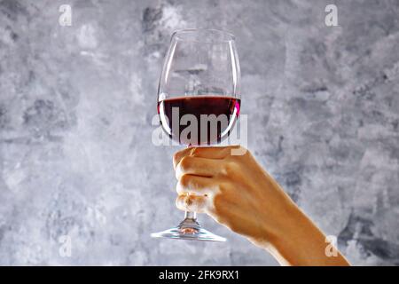 Nahaufnahme von weiblichen Armen wirbelnden Weinglas mit teuren Pinot Noir Wein in einer Hand gegen Licht grunged Betonwand Hintergrund. Zugeschnittenes Bild, CO Stockfoto